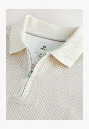 Kortærmet, lysefarvet zip-polo med struktureret krave og ternet mønster. Etiketten viser "NEXT", størrelse M, med sølvfarvet lynlåsdetalje.