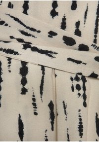 Primo piano di un tessuto crema con macchie astratte nere irregolari e motivi a pennellate, con un dettaglio di cucitura e una cintura piegata.