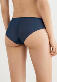 Culottes hipster bleu marine en tissu lisse, avec une coupe sans couture et des détails de couture subtils. Ajustement réglable au niveau de la taille.