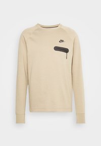 Beżowa bluza Nike z długim rękawem, z czarną zamkiem kieszenią na klatce piersiowej i logo Nike po lewej stronie, o okrągłym dekolcie.