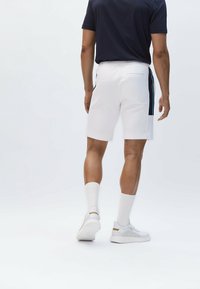 Bílé šortky s postranním námořnickým pruhem, elastickým pasem a zadní kapsou; v kombinaci s námořnickým tričkem a bílými ponožkami a botami.