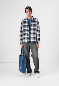 Rutete flanellskjorte i marineblå og hvit; kombinert med en blå T-skjorte og grå jeans. Holder en blå denim tote-bag. Hvit sneakers.