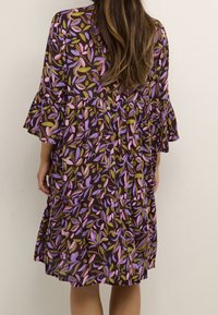 Vestido marrón con diseño de volantes, con un patrón floral en púrpura, rosa y verde. Mangas acampanadas y tela ligera.