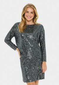 Vestido de lentejuelas plateadas con mangas largas y escote redondo. La tela tiene una textura brillante y una silueta ajustada.
