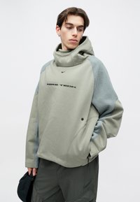 Oversized φούτερ από μαλακό πράσινο ύφασμα με γκρι μανίκια τύπου fleece. Διαθέτει ψηλό γιακά, λογότυπο μπροστά και ρυθμιζόμενο κορδόνι.