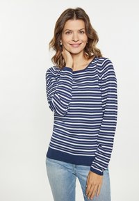 Maglione a righe navy e bianche con maniche lunghe, scollatura rotonda e polsini a costine. Indossato con jeans azzurri chiari, presenta una texture liscia.