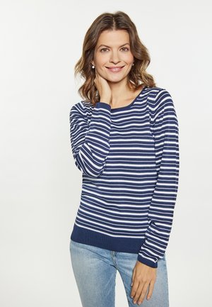 Maglione a righe navy e bianche con maniche lunghe, scollatura rotonda e polsini a costine. Indossato con jeans azzurri chiari, presenta una texture liscia.