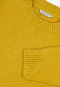 Gelber Strickpullover aus weichem Material, mit rundem Halsausschnitt und gerippten Bündchen. Enthält eine aufgesetzte Tasche auf der Vorderseite.