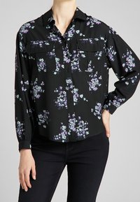 Svart blommig skjorta med knappar som pryds av lila och turkosa blommor, två framfickor och långa ärmar med knäppte manschetter, tillverkad av lättviktsmaterial.