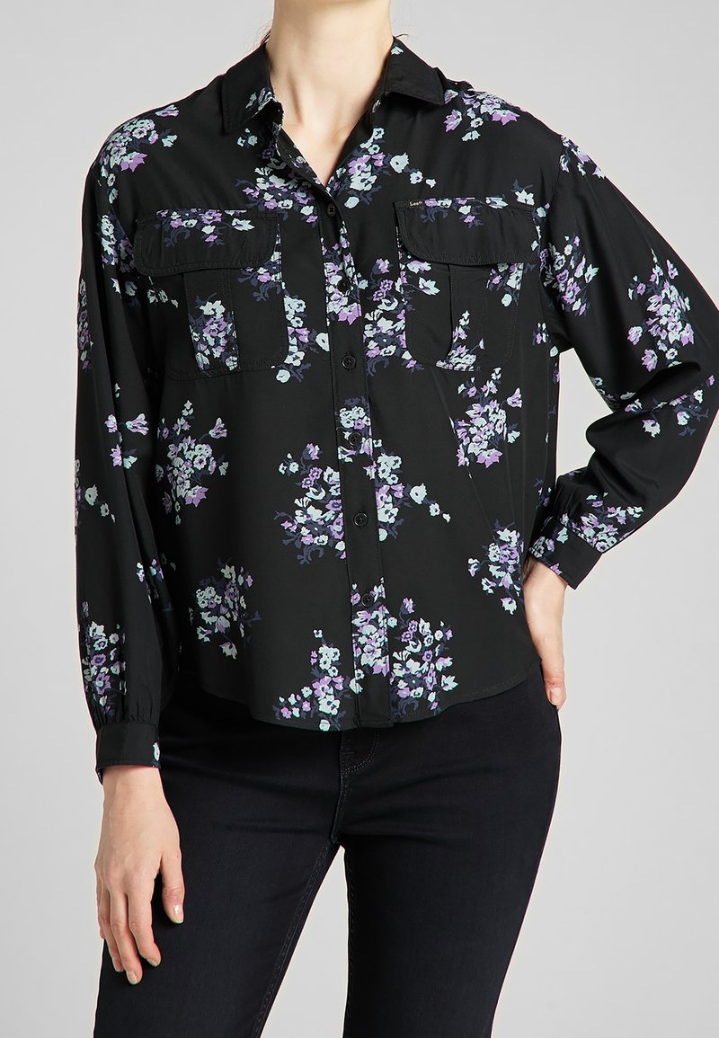 Svart blommig skjorta med knappar som pryds av lila och turkosa blommor, två framfickor och långa ärmar med knäppte manschetter, tillverkad av lättviktsmaterial.