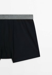 Black boxer shorts made of soft fabric, featuring a gray elastic waistband. Seam detailing along the sides adds visual texture.