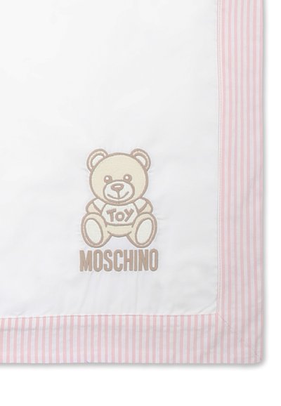 Witte deken met een roze gestreepte rand, met een geborduurde teddybeer en de tekst "MOSCHINO" onder de beer. Zachte stoftextuur.