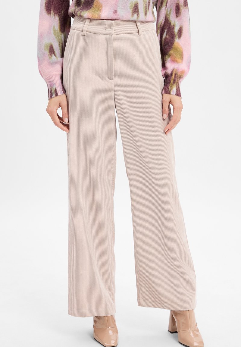 Pantalon large en velours côtelé beige porté avec un haut multicolore à manches longues et des bottines nude vernis à talons carrés.