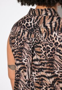 Ärmelloses Shirt mit Leopardenmuster aus einem weichen, glatten Material; mit Kragen und einem dezenten Faltendetail auf der Rückseite.