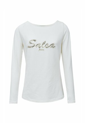 Camiseta blanca de manga larga con un escote amplio que presenta "Salsa" en rhinestones plateados y "Jeans" en bordado dorado debajo. Textura de tejido suave.