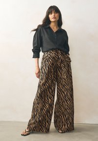 Camisa negra de corte amplio con botones, combinada con pantalones de pierna ancha con un estampado de rayas de tigre en marrón y negro y bolsillos laterales.