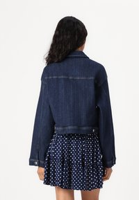 Mørkeblå denimjakke med croppet design, med klassisk krage, lange ermer og to knapper bak. Strukturert overflate.