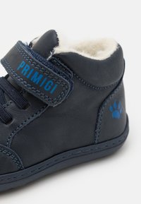 Laivansinis nahkainen nilkkuri, softaa sisävuorta, nauhoitus, Velcro-hihna ja sininen logo; sisältää tassunjälkiakcentin kantapäällä.