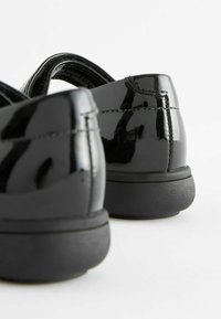 Schwarze Lacklederschuhe mit abgerundeten Fersen, niedrigen Gummisohlen und minimalen Nähdetails. Glatte, glänzende Oberfläche.