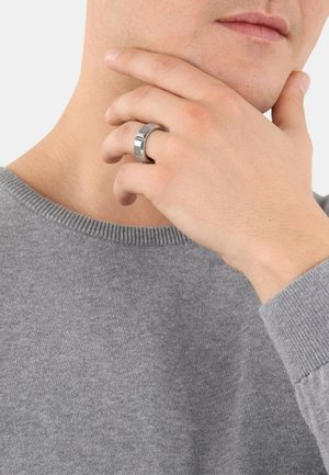 Metalowy pierścień o eleganckim, wypolerowanym srebrnym wykończeniu. Noszony na palcu, ukazuje gładką, zaokrągloną obrączkę i nowoczesny design.