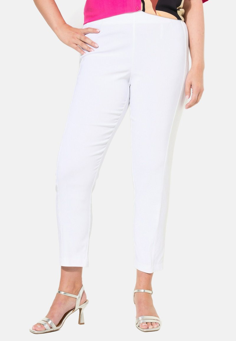 Pantalons slim-fit blancs avec une texture lisse et un design sur mesure. Assortis à des sandales à talons métalliques pour créer un contraste.