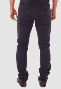 Jeans de mezclilla oscura con un corte ajustado, que presentan bolsillos traseros con remaches de cobre, y combinados con zapatillas negras y una cinturilla texturizada.