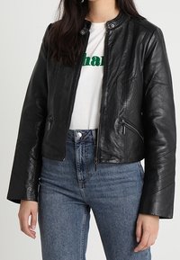 Černá kožená zkrácená bunda s kulatým výstřihem, předním zipem a dvěma bočními kapsami; má vertikální švy a hladkou strukturu.