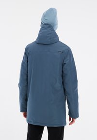 Veste imperméable bleue avec col haut et capuche ajustable. Fabriquée en matériau lisse et léger, avec un logo dans le dos.