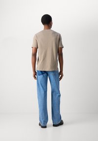 T-shirt beige a maniche corte con collo rotondo, abbinato a jeans di denim blu larghi. Le scarpe nere completano l'outfit. Design pulito e semplice.