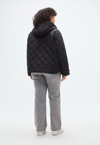 Μαύρο καπιτονέ μπουφάν με κουκούλα, με μοτίβο διαμαντιού. Φορεμένο με ανοιχτό γκρι παντελόνι φαρδιάς γραμμής και λευκά αθλητικά παπούτσια. Απλός, μινιμαλιστικός σχεδιασμός.