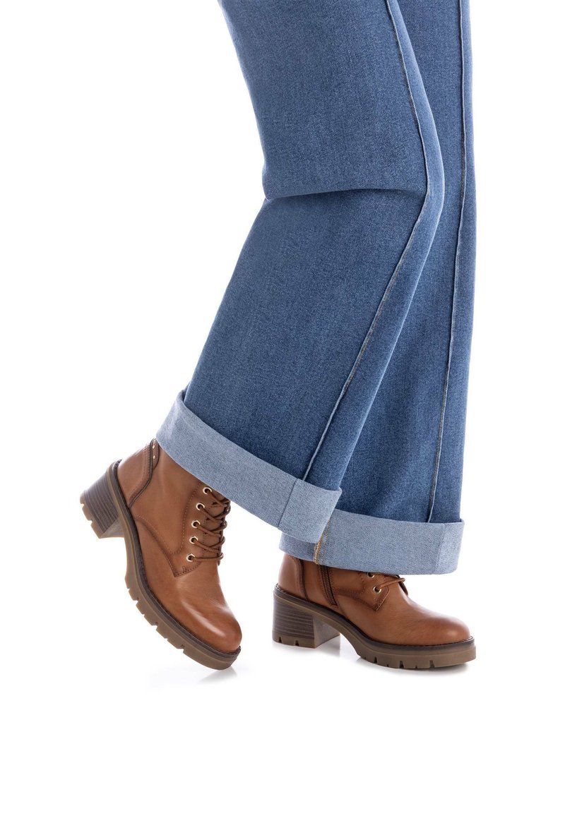 Botas de cuero marrón hasta el tobillo con diseño de cordones, resistentes tacones cuadrados y suelas texturizadas, combinadas con pantalones de denim azul claro con dobladillos.