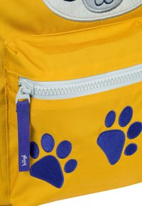 Zaino in tessuto giallo con cerniera bianca, caratterizzato da ricami di impronte di zampe blu sulla tasca frontale e un tirante della cerniera viola.