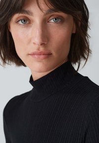 Maglione a dolcevita nero a coste con collo alto e design aderente, caratterizzato da una texture liscia e sottili linee verticali.