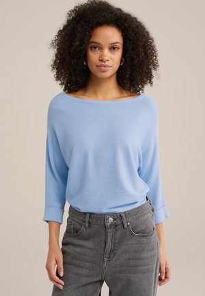 Ljust blå ribbad topp med båthals och trekvartslånga ärmar, tillsammans med högmidjade grå jeans. Texturen är mjuk och avslappnad.