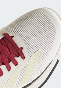 Sneaker con una toma in rete off-white testurizzata, lacci cremisi e sottili accenti gialli; presenta una suola in gomma contornata.