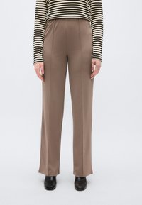 Calças largas castanhas feitas de tecido suave, com cintura alta e vinco central subtil, combinadas com um top às riscas preto e bege.