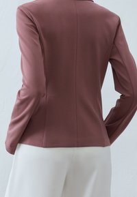 Rosa kavaj i figurnära snitt med lång ärm, slät textur och skräddarsydd form, i kombination med vita byxor.