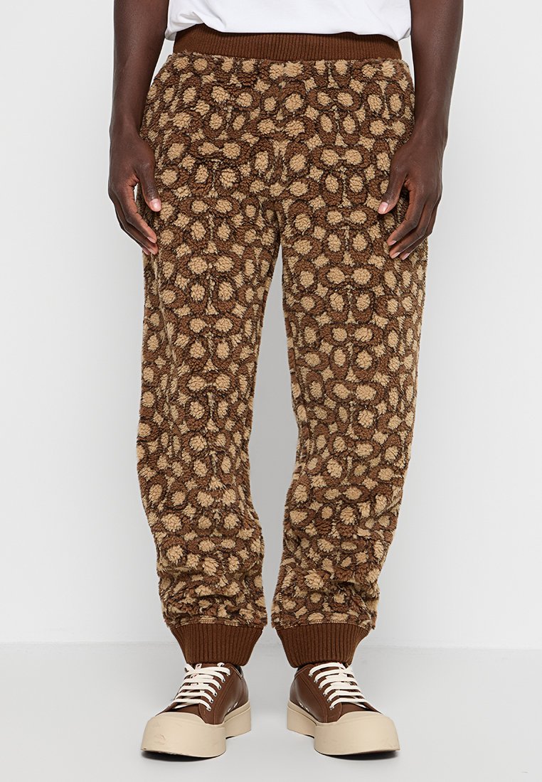 Brązowe, puszyste spodnie dresowe w wzór lamparta, z ribbowanym pasem i mankietami, zestawione z jasnobrązowymi, sznurowanymi trampkami.