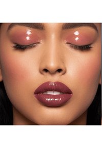 Close-up van een gezicht met glanzende mauve lippen, glanzende roze oogleden en subtiele blush op de wangen, met een egale huidtextuur en goed gedefinieerde wenkbrauwen.
