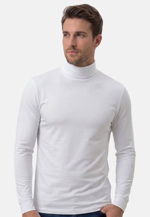 Mann mit kurzem braunem Haar und leichtem Bart, der ein eng anliegendes weißes Langarmshirt mit Rollkragen trägt und nach links schaut.