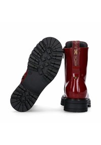 Stivali alla caviglia in pelle sintetica rossa con suola in gomma nera spessa, dotati di zip laterale e di un accento con logo sul tallone posteriore.