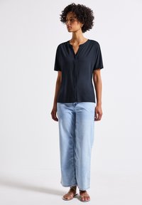 Camicia nera a maniche corte con bottoni, realizzata in un tessuto morbido, abbinata a jeans a gamba larga blu chiaro e sandali argento con lacci.