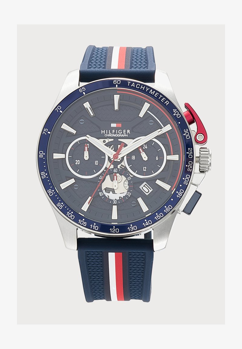 Ρολόι χρονογράφου Tommy Hilfiger με μπλε καντράν και λουράκι, λευκές και κόκκινες λεπτομέρειες, ταχύμετρο στεφάνη και τρεις υποκαντράν που δείχνουν λειτουργίες ώρας.