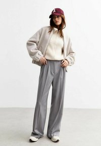 Överdimensionerad beige fleecejacka, ribbad krämfärgad tröja, grå skräddarsydd byxor, vinröd keps med bokstavsdetalj, vita sneakers.
