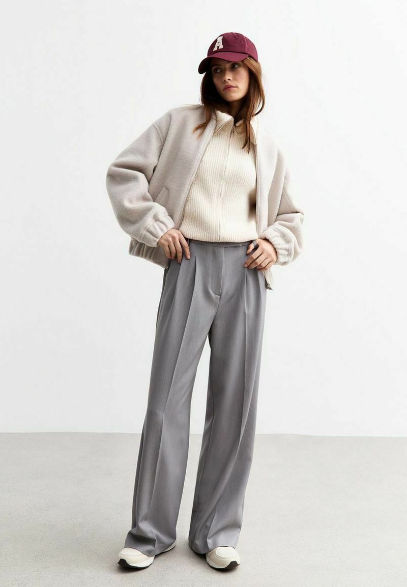 Överdimensionerad beige fleecejacka, ribbad krämfärgad tröja, grå skräddarsydd byxor, vinröd keps med bokstavsdetalj, vita sneakers.