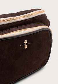 Brown suede bag with gold-tone zipper and accents. Rounded shape, double zip opening, and light beige piping along the edge.