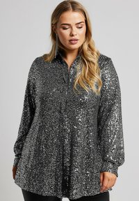 Blusa nera e argento con paillettes, maniche lunghe, design con colletto e vestibilità ampia. Presenta una texture lucida e una chiusura con bottoni davanti.