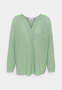 Blusa verde chiaro a maniche lunghe con scollatura a V, tessuto testurizzato, vestibilità rilassata e pieghe sottili sul davanti. Presenta un logo laterale.