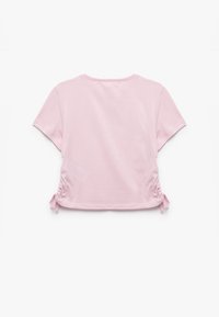 Camiseta cropped rosa hecha de una tela suave, con mangas cortas, escote redondo y detalles fruncidos en los laterales con lazos ajustables.