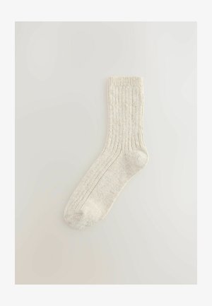 Térdig érő, krém színű, bordázott zokni, puha, textúrált anyagból, megerősített lábfejjel és szegéllyel a tartósság érdekében.